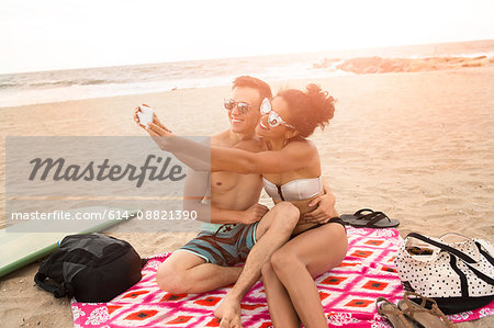 Young couple taking smartphone selfie on Rockaway Beach, New York State, USA