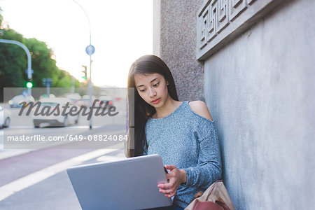 Young woman on sidewalk using laptop