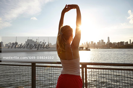 Rear view of woman on pier arms raised stretching, Manhattan, New York, USA