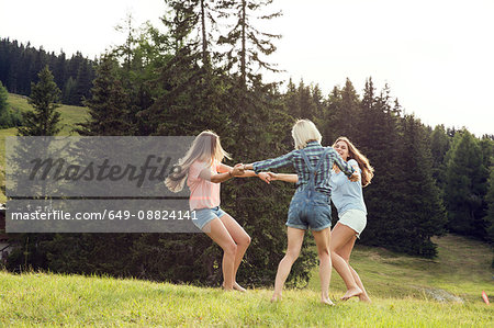 Three female adult friends playing ring-a-rosie in field, Sattelbergalm, Tirol, Austria