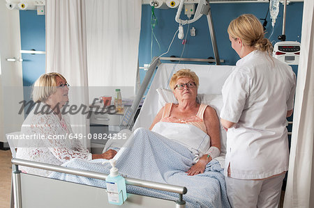 Nurse and visitor tending to patient in hospital bed