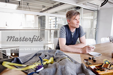 Fashion designer at table holding tea cup looking away