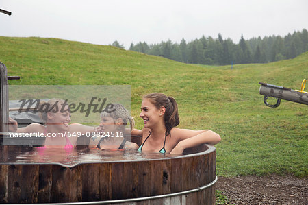 Three female friends laughing whilst relaxing in rural hot tub, Sattelbergalm, Tyrol, Austria