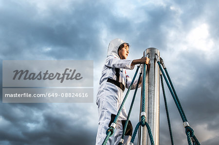 Boy in astronaut costume gazing from top of climbing frame against dramatic sky