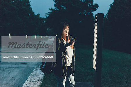 Young woman reading smartphone texts in park at night