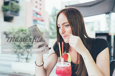 Young woman at sidewalk cafée reading smartphone texts