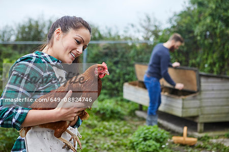 Young couple in chicken coop holding chicken