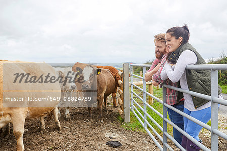 Couple leaning against gate on cow farm looking away