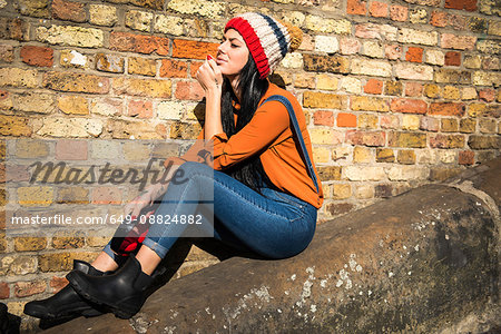 Young woman sitting on wall, holding earphones