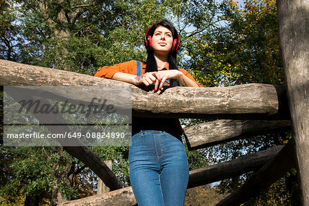 Young woman resting on wooden climbing frame, wearing headphones