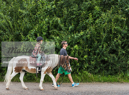 Side view of father guiding daughter riding horse