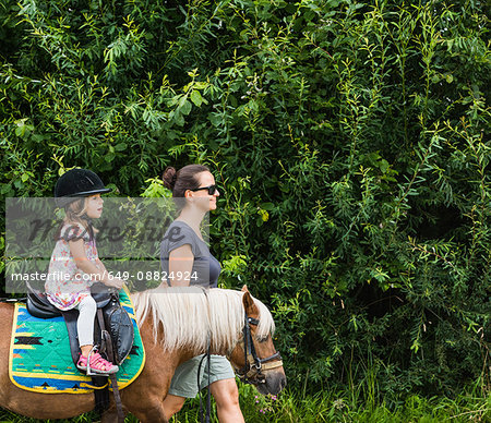 Side view of mother guiding daughter riding horse