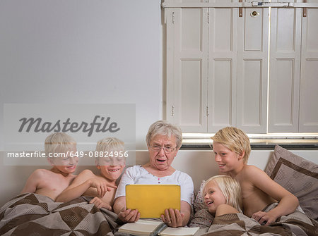 Grandmother in bed with grandsons using digital tablet