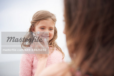 Mother applying sun cream on daughter's cheek