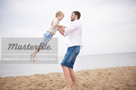 Father swinging son on beach