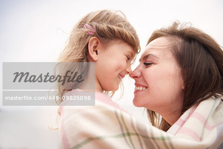 Happy mother and daughter wrapped in blanket, rubbing noses