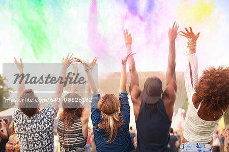 Group of friends at festival, throwing colourful powder paint in air, rear view