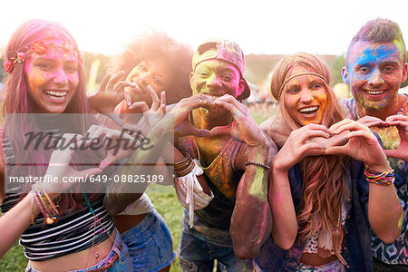 Portrait of group of friends at festival, covered in colourful powder paint, making heart shapes with hands