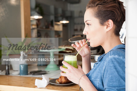 Young woman sitting at bar in cafée, drinking drink through straw
