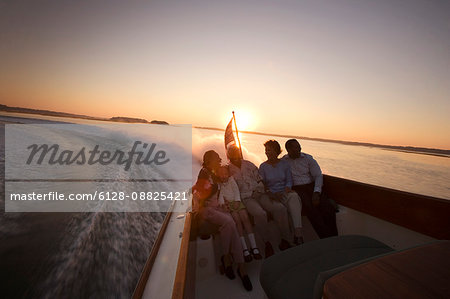 Happy family sitting in the back of a jet boat on the water at sunset.