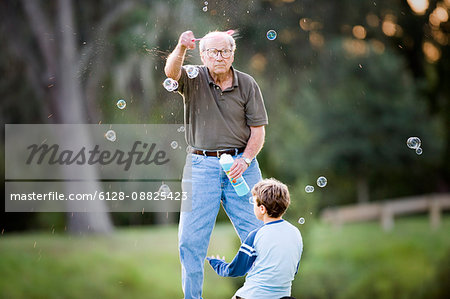 Senior adult man making bubbles for his young grandson outside at sunset.