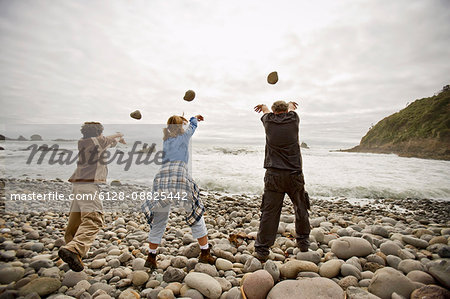 Mature man with his teenage grandchildren throwing rocks into the sea.