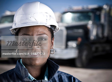 Portrait of female worker in hard hat in front of recycling plant trucks