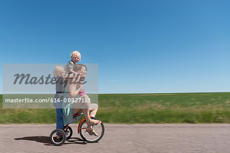 Side view of mother and children riding tricycle in rural area