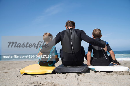Rear view of man and two sons sitting on bodyboards, Laguna Beach, California, USA