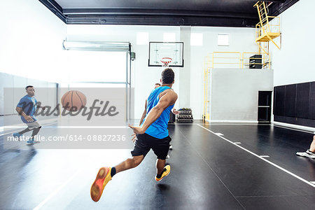 Two male basketball players running and passing ball on basketball court