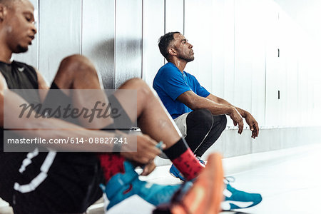 Exhausted male basketball players taking a break on changing room floor