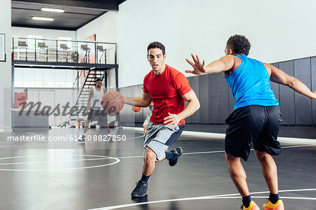 Two male basketball players practicing running and defending ball on basketball court