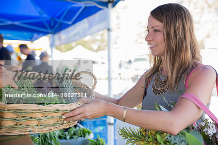 Woman at fruit and vegetable stall receiving basket of fresh herbs