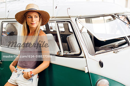 Woman leaning against vintage camper van looking away