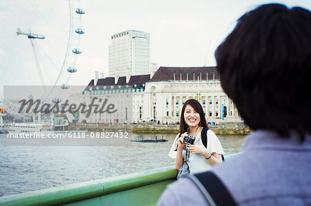 Young Japanese man and woman enjoying a day out in London, standing by the River Thames, London Eye in the background.