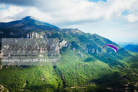 A paraglider in flight over a valley in the mountains.