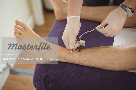 Physiotherapist performing electro dry needling on the leg of a patient