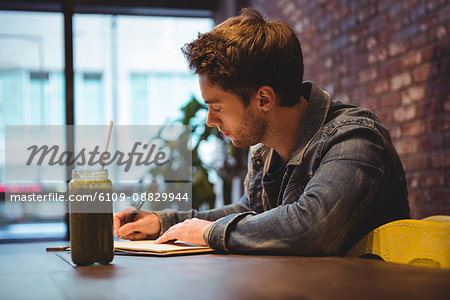 Man writing in his dairy with juice on table