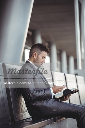 Businessman with a diary using mobile phone while sitting on a bench