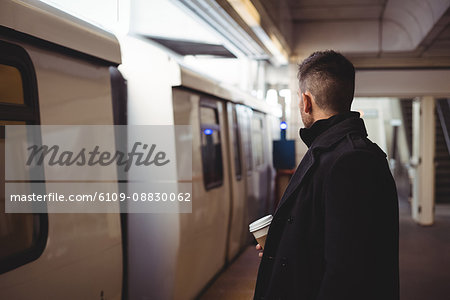 Businessman with a disposable coffee cup waiting for train
