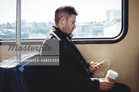 Businessman holding a disposable coffee cup and listening to music on mobile phone