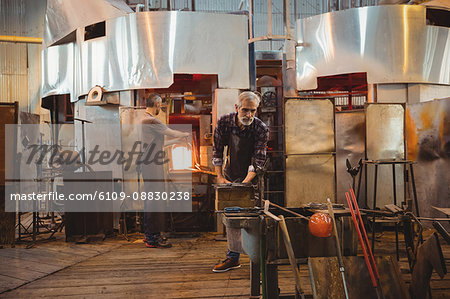 Team of glassblowers shaping a glass on the blowpipe