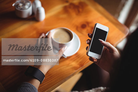 Woman using mobile phone while having a cup of coffee