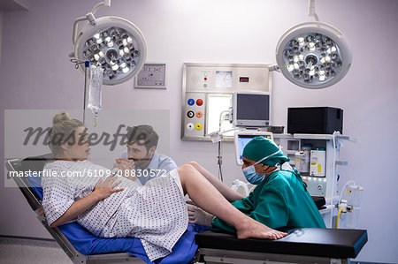 Doctor examining pregnant woman during delivery while man holding her hand in operating room