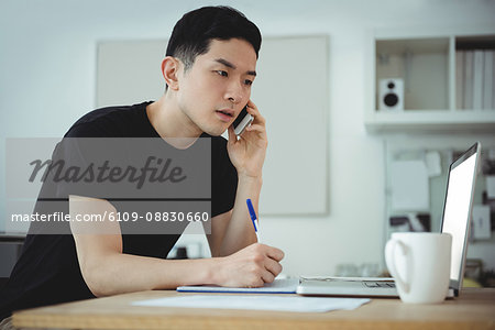 Business executive writing on diary while talking on mobile phone