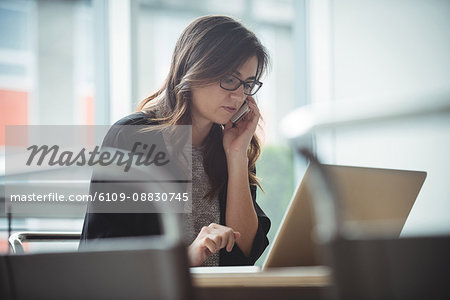Business executive talking on mobile phone while using laptop