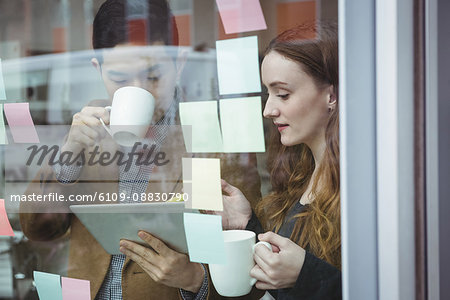 Business executives discussing over digital tablet while having cup of coffee