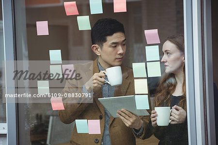 Business executives discussing over digital tablet while having cup of coffee