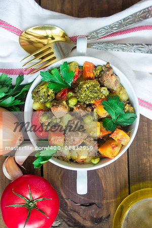 served beef meat stewed with potatoes, carrots and spices in ceramic pot with ingredients on wooden background. vertical
