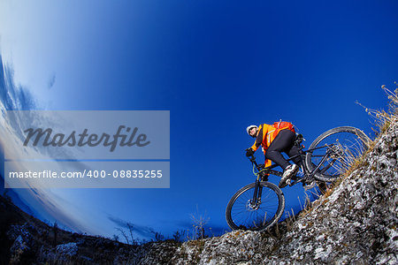 Mountain biker in action across rocks against blue sky concept for healthy lifestyle, exercise and extreme sports